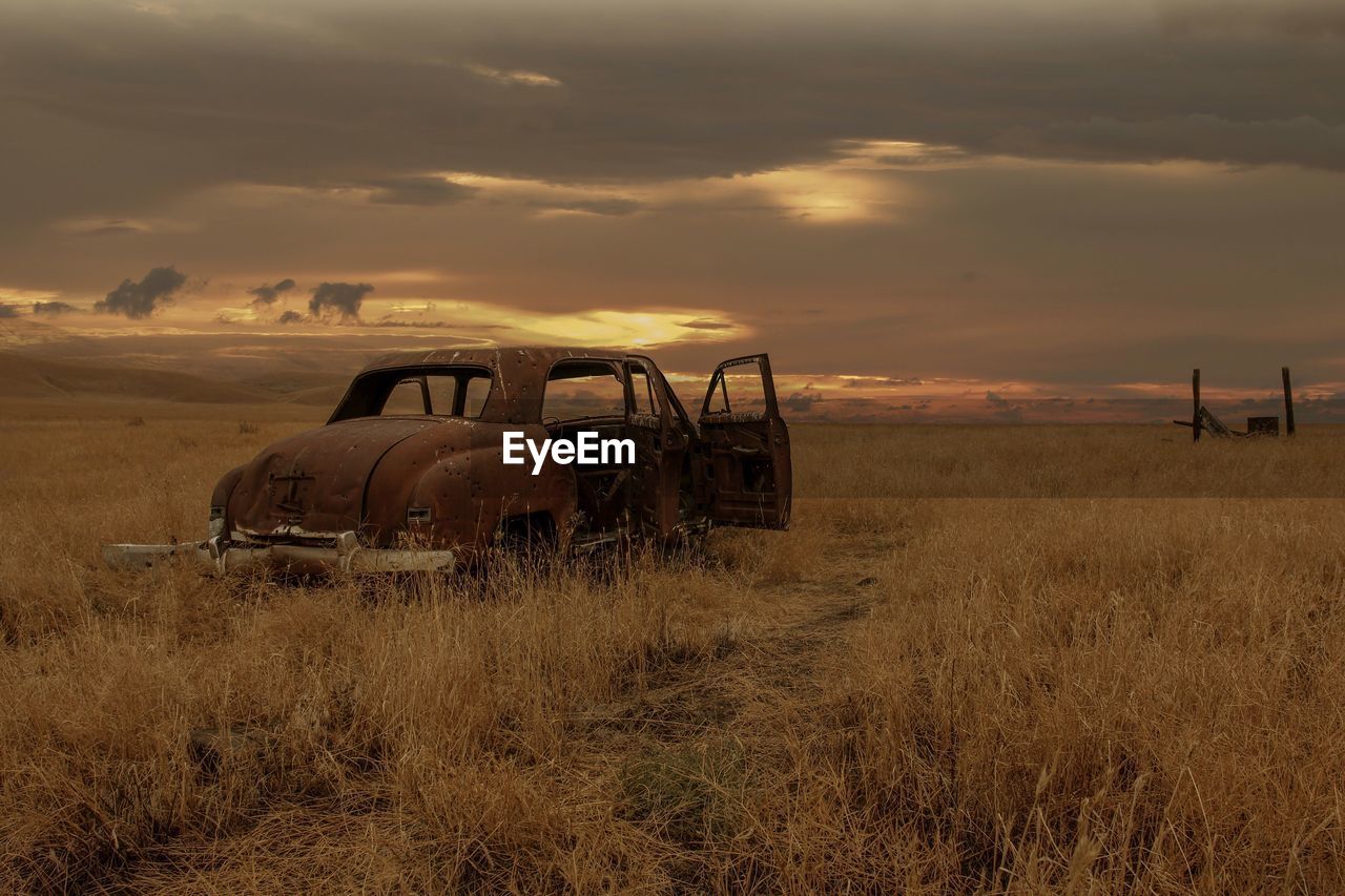 Abandoned vintage car on field against sky during sunset