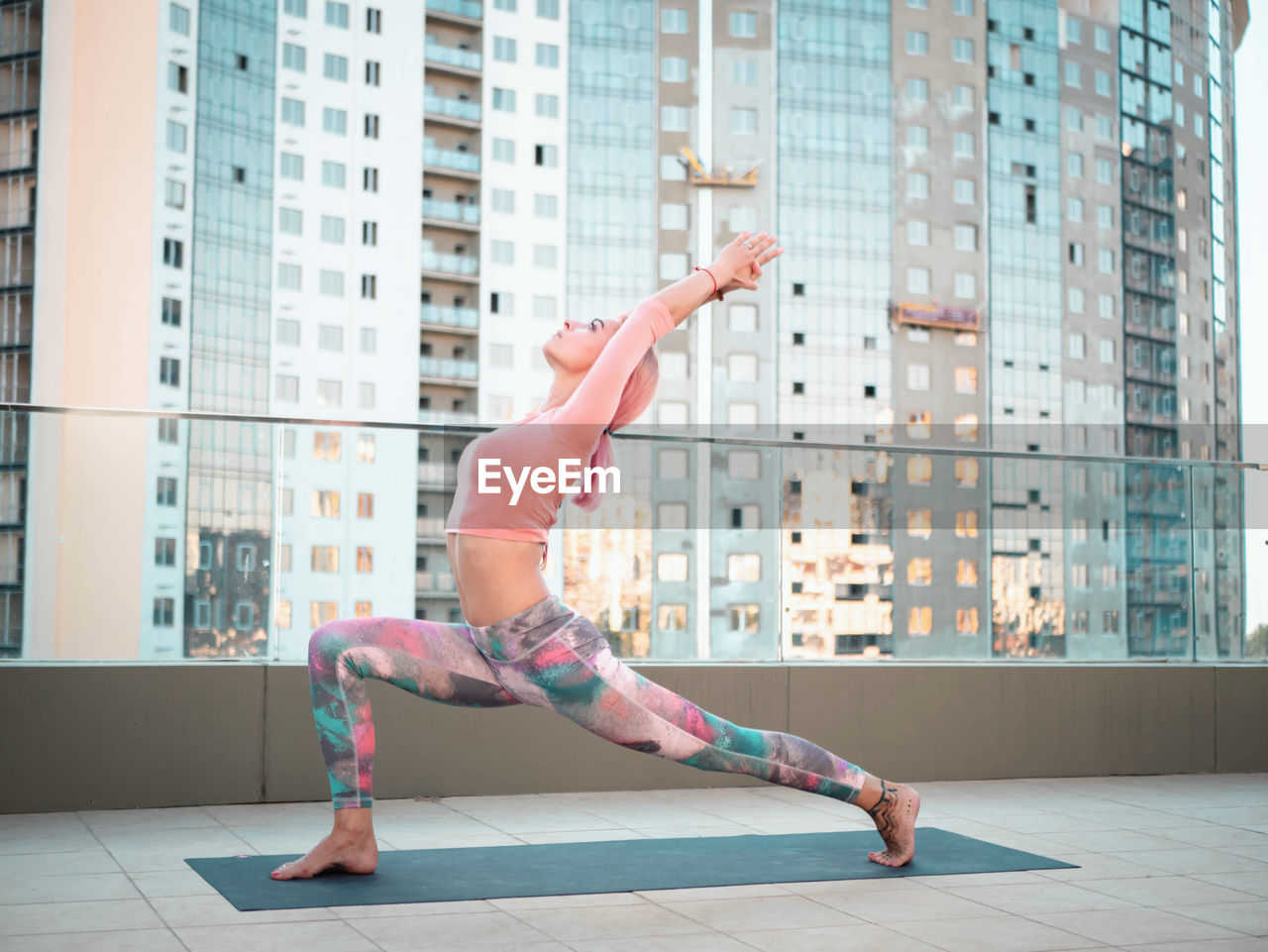 Full length of young woman exercising yoga on building terrace in city