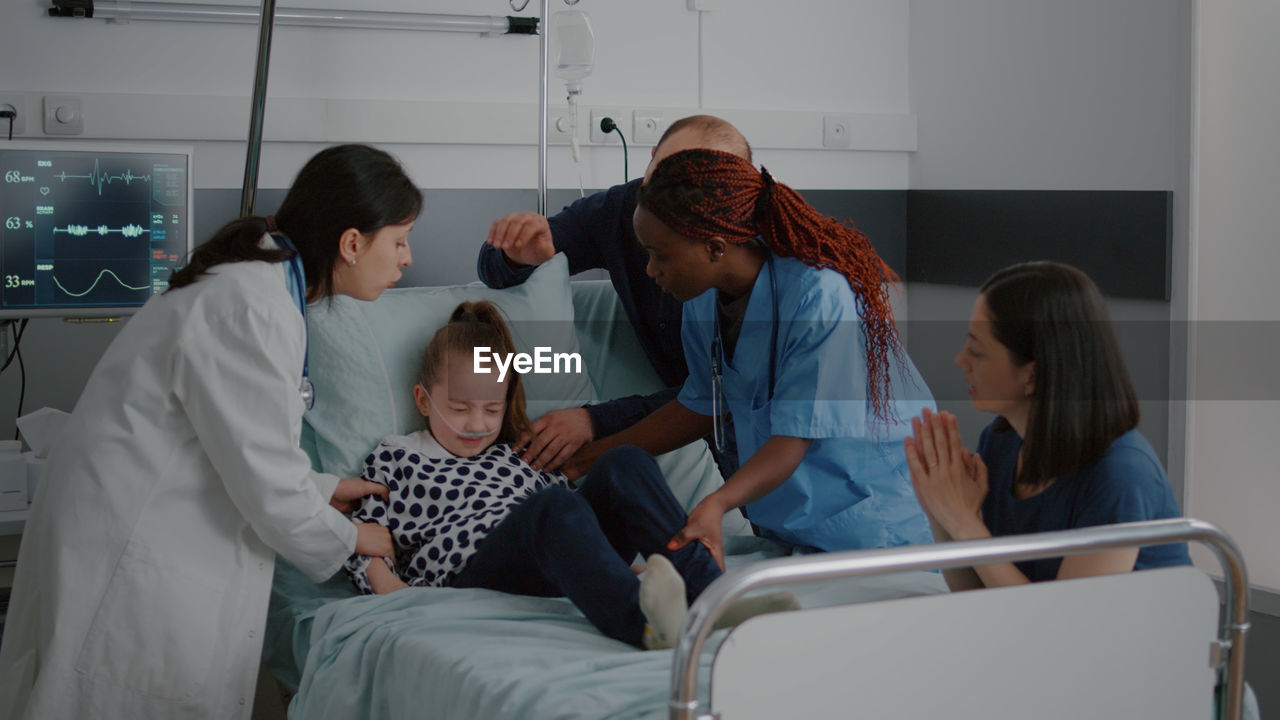 Doctor and parent assisting girl on bed at hospital