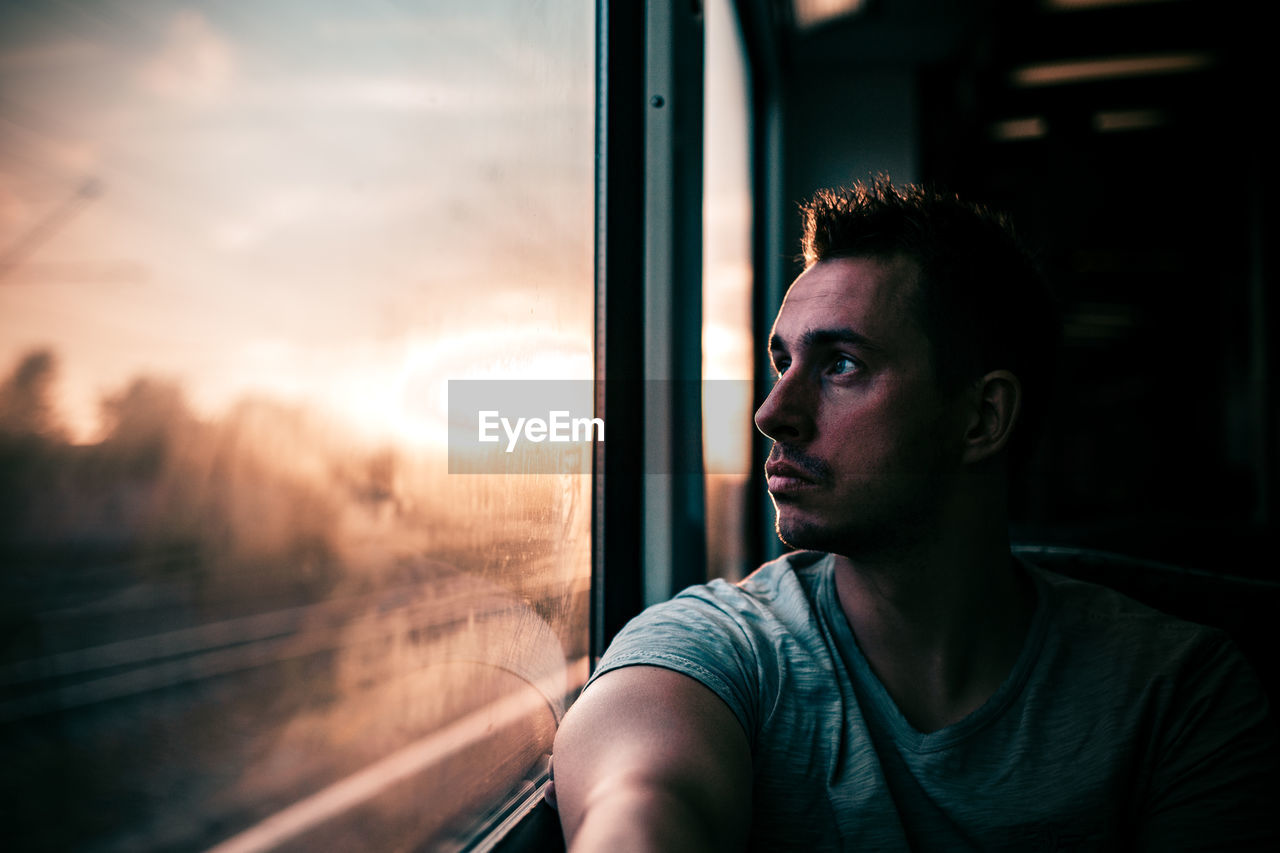 Young man looking through train window during sunset