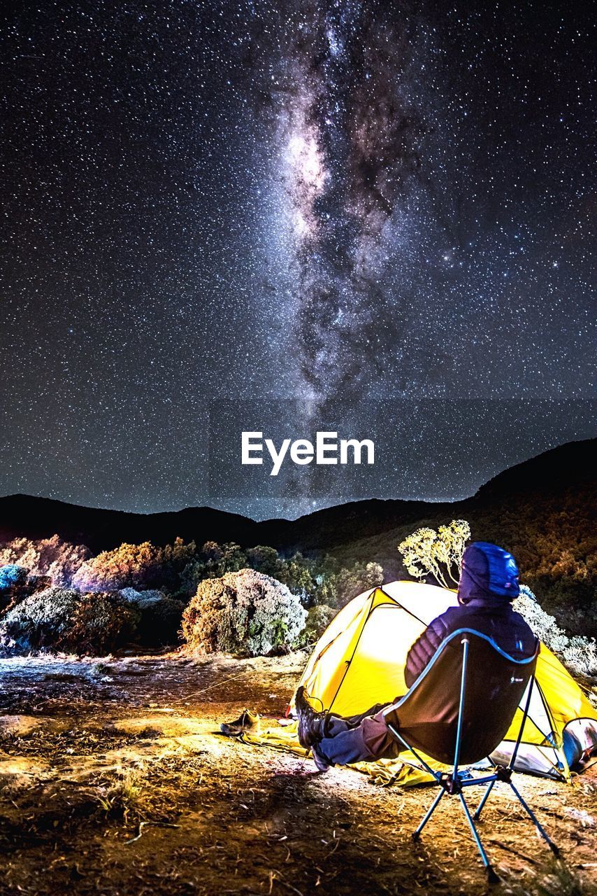 Person sitting by tent against star field at night