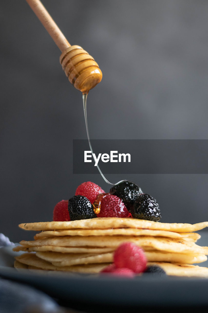 Pouring raw honey over homemade crepes on table, dark food photography