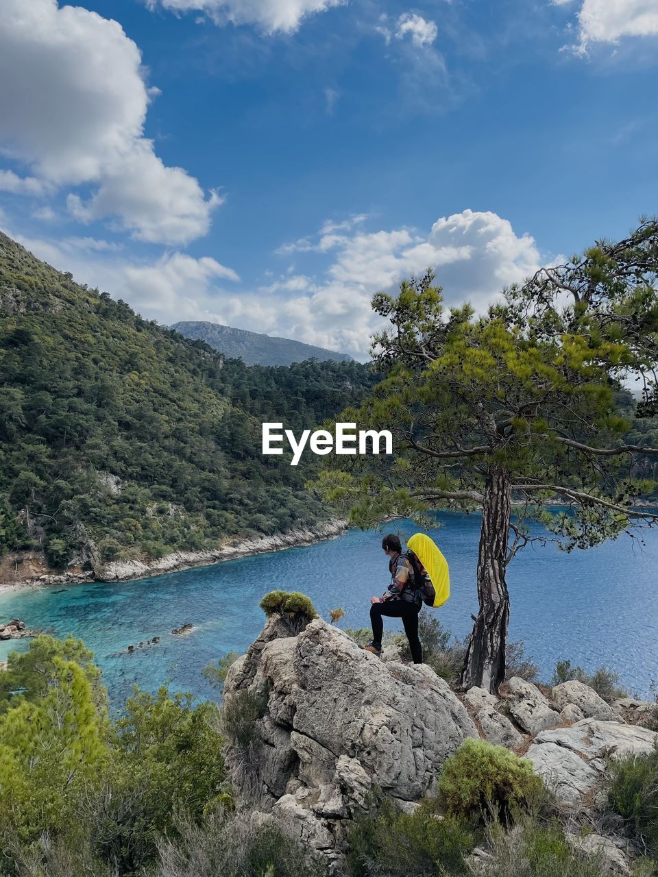 mountain, leisure activity, water, nature, wilderness, activity, sky, tree, beauty in nature, rock, scenics - nature, plant, adventure, cloud, adult, hiking, men, full length, environment, holiday, vacation, travel, trip, one person, land, day, lifestyles, backpack, landscape, mountain range, lake, travel destinations, outdoors, exploration, forest, non-urban scene, tranquility, sports, tranquil scene, recreation, tourism, walking, outdoor pursuit, pinaceae, coniferous tree, blue, women, climbing, person, weekend activities, remote