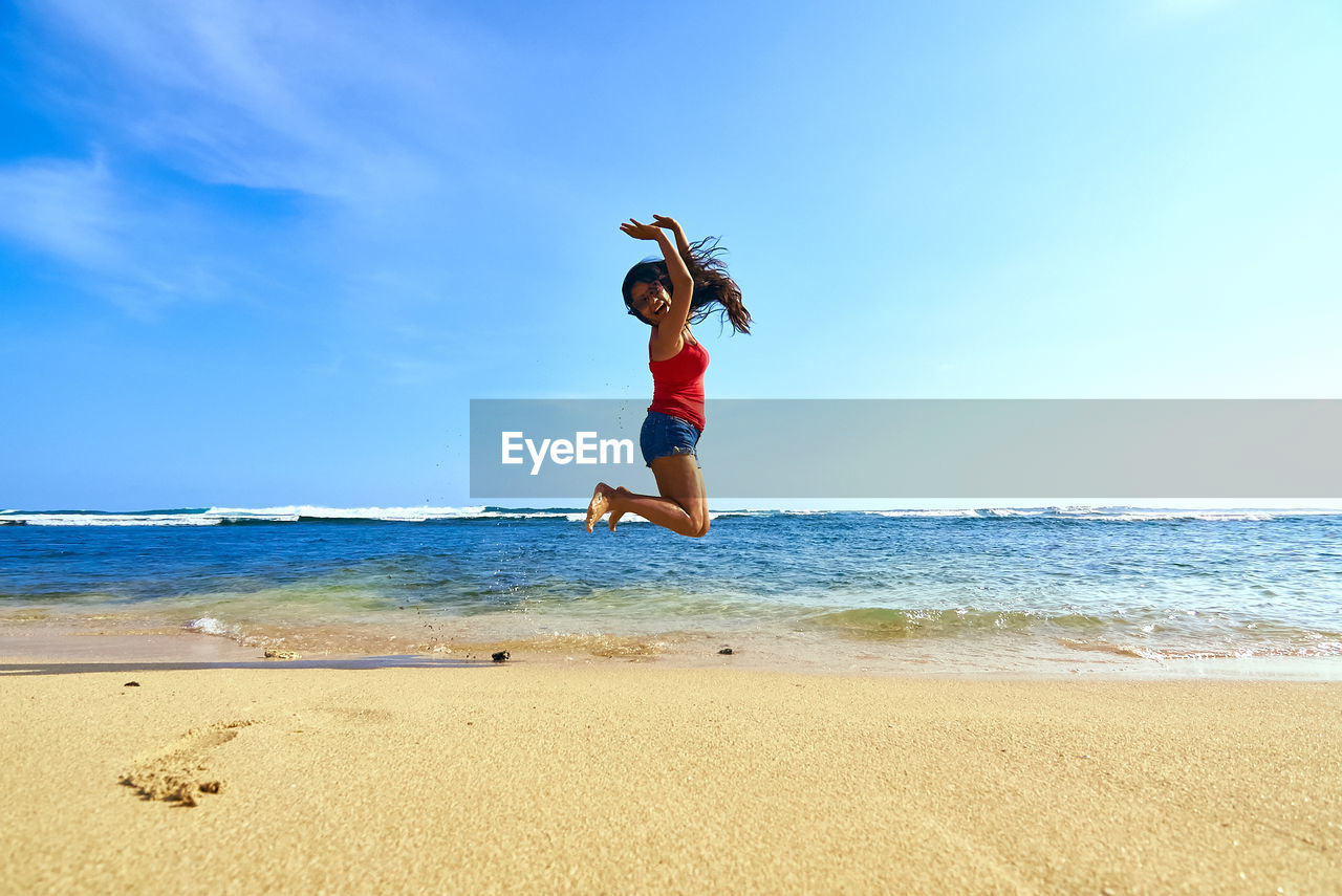 Full length of woman jumping at beach against sky