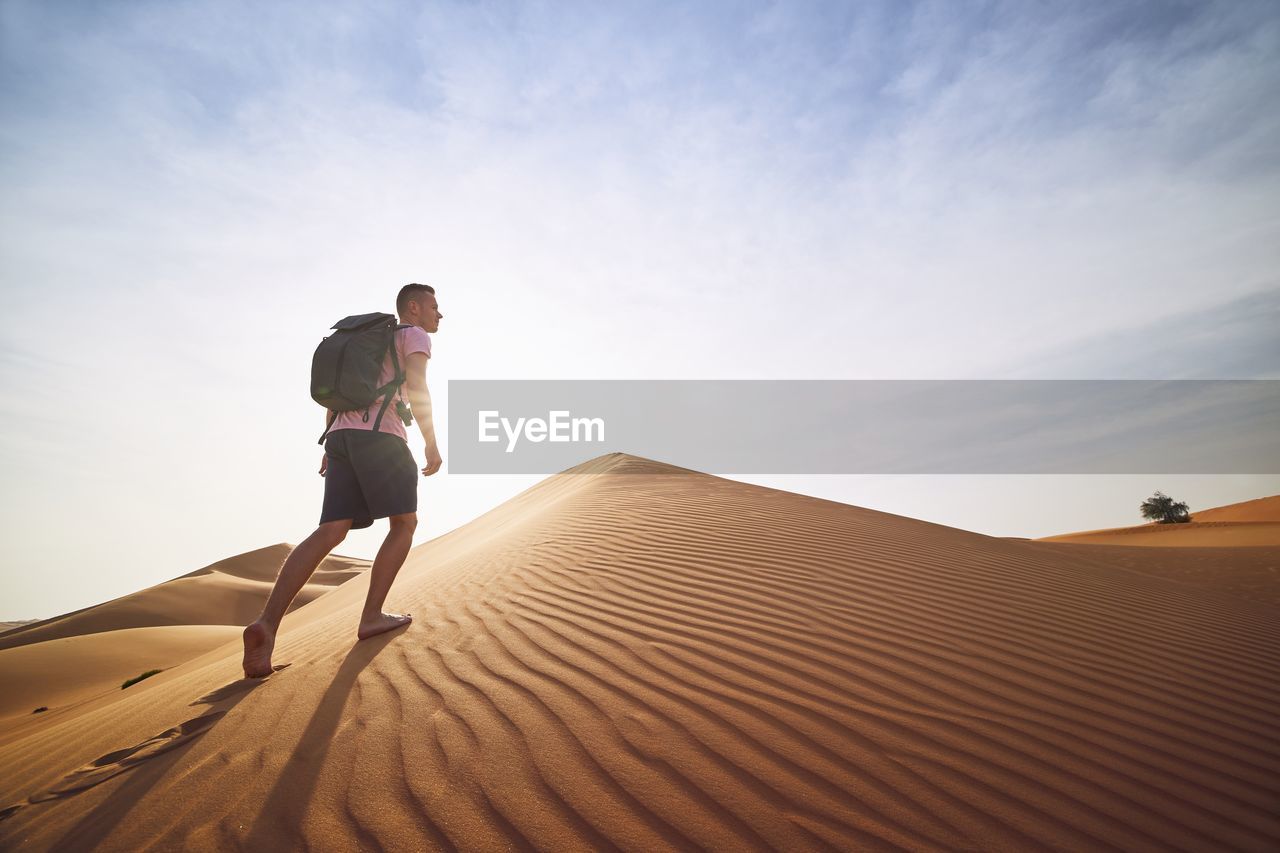 Low angle view of man walking on sand dunes at desert against sky