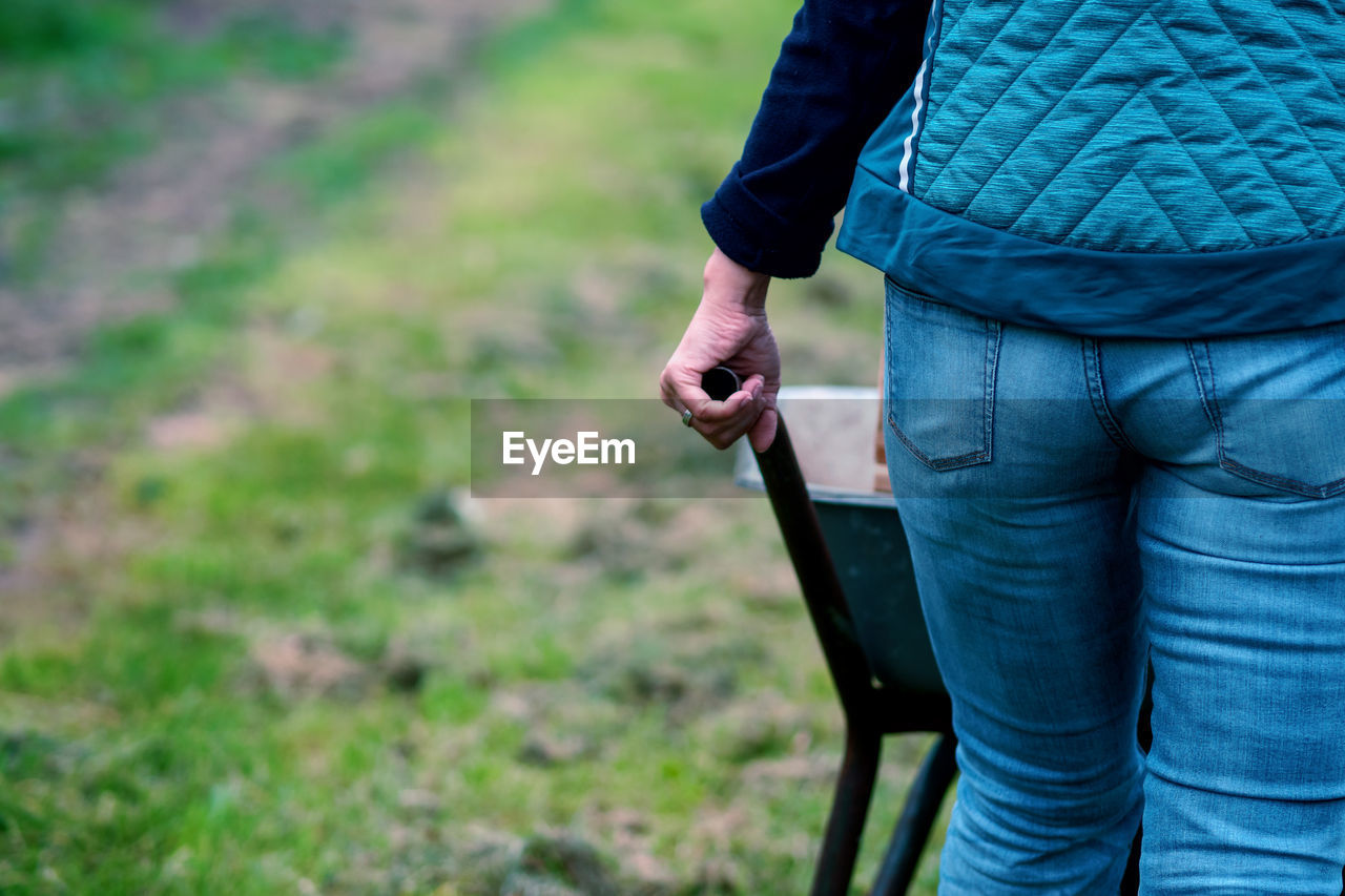 Midsection of woman pushing wheel barrow on field