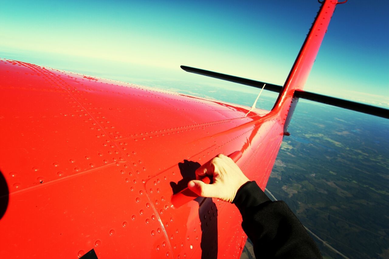 Cropped hand holding red airplane handle flying in sky