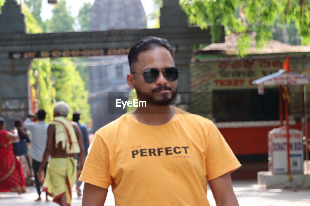 sunglasses, fashion, glasses, portrait, one person, focus on foreground, architecture, men, front view, adult, waist up, young adult, day, looking at camera, t-shirt, standing, casual clothing, city, outdoors, lifestyles, person, sunlight, clothing, leisure activity, cool attitude, beard, nature, arts culture and entertainment, spring