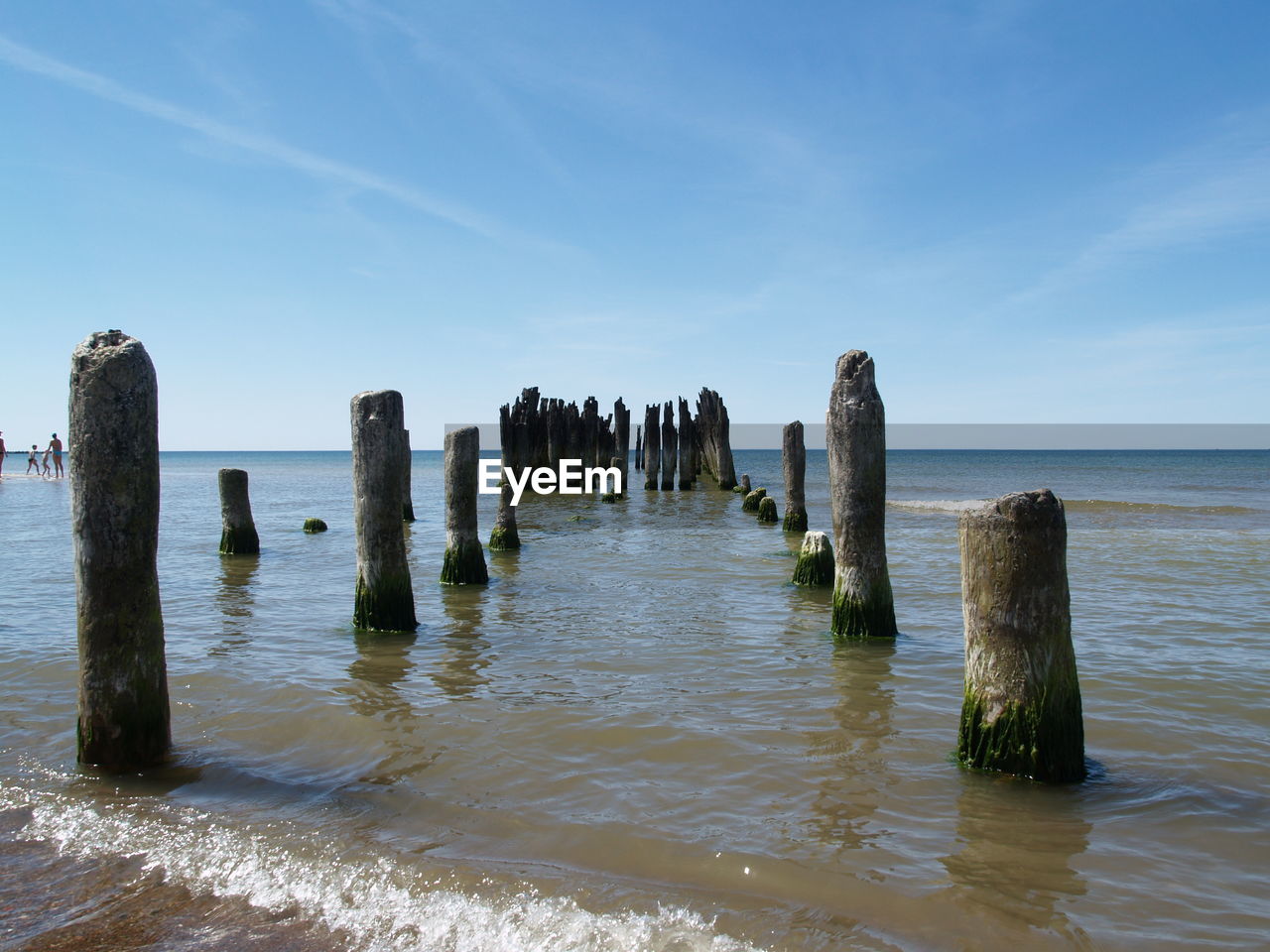 Wooden posts in sea against sky