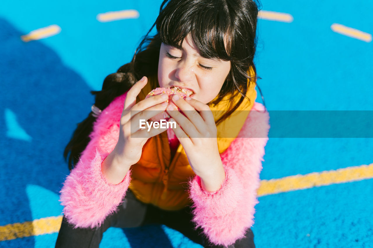 Cute girl eating donut while sitting on basketball court