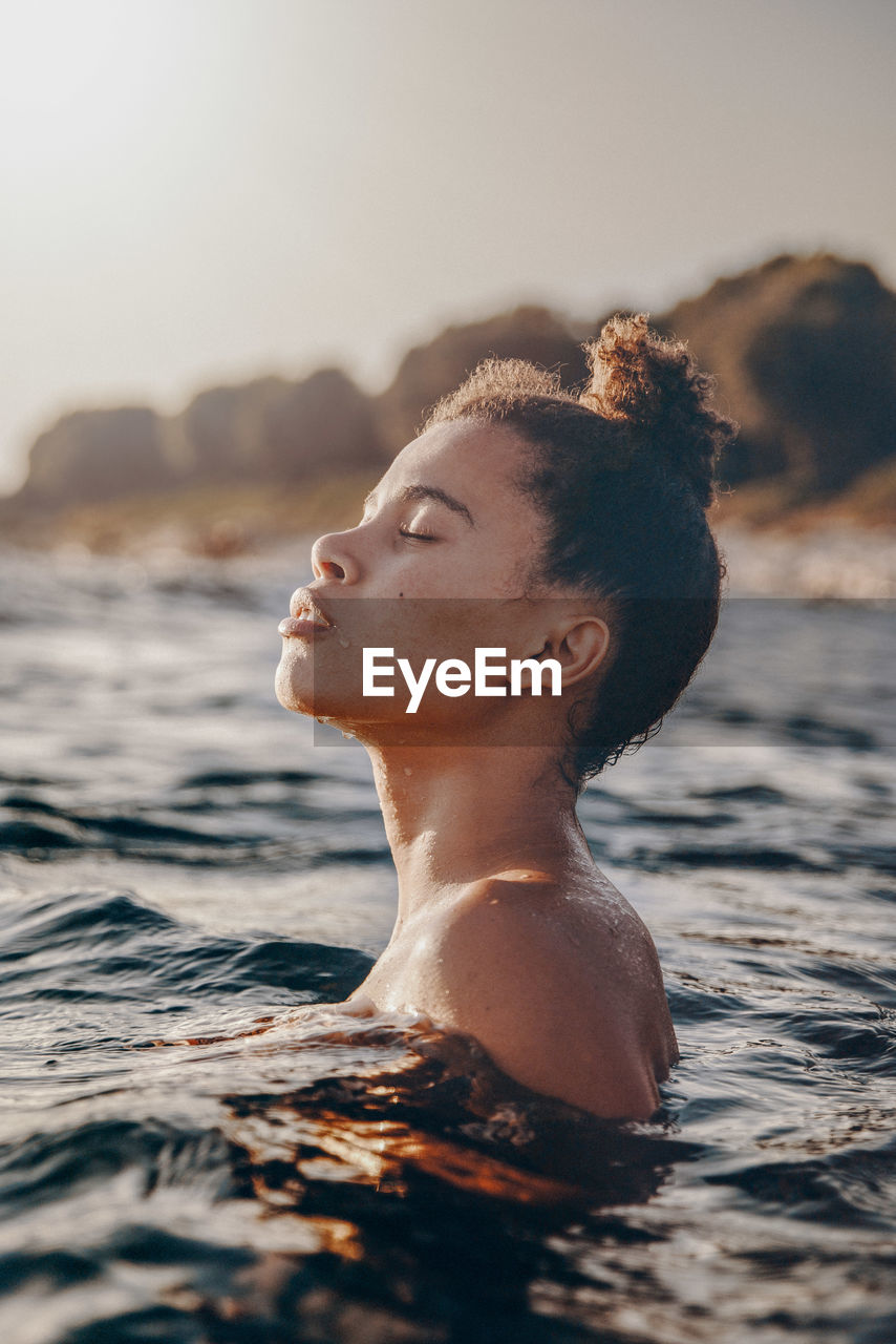 Side view of woman in sea against sky during sunset