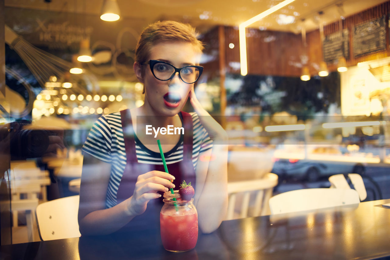 Portrait of surprised woman drinking cocktail at cafe