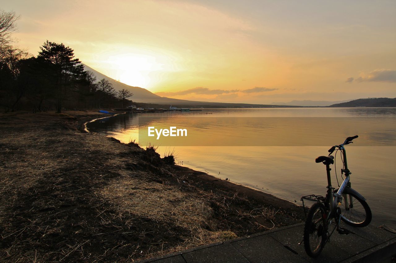 Bicycle by lake against sky and snowcapped volcano during sunset