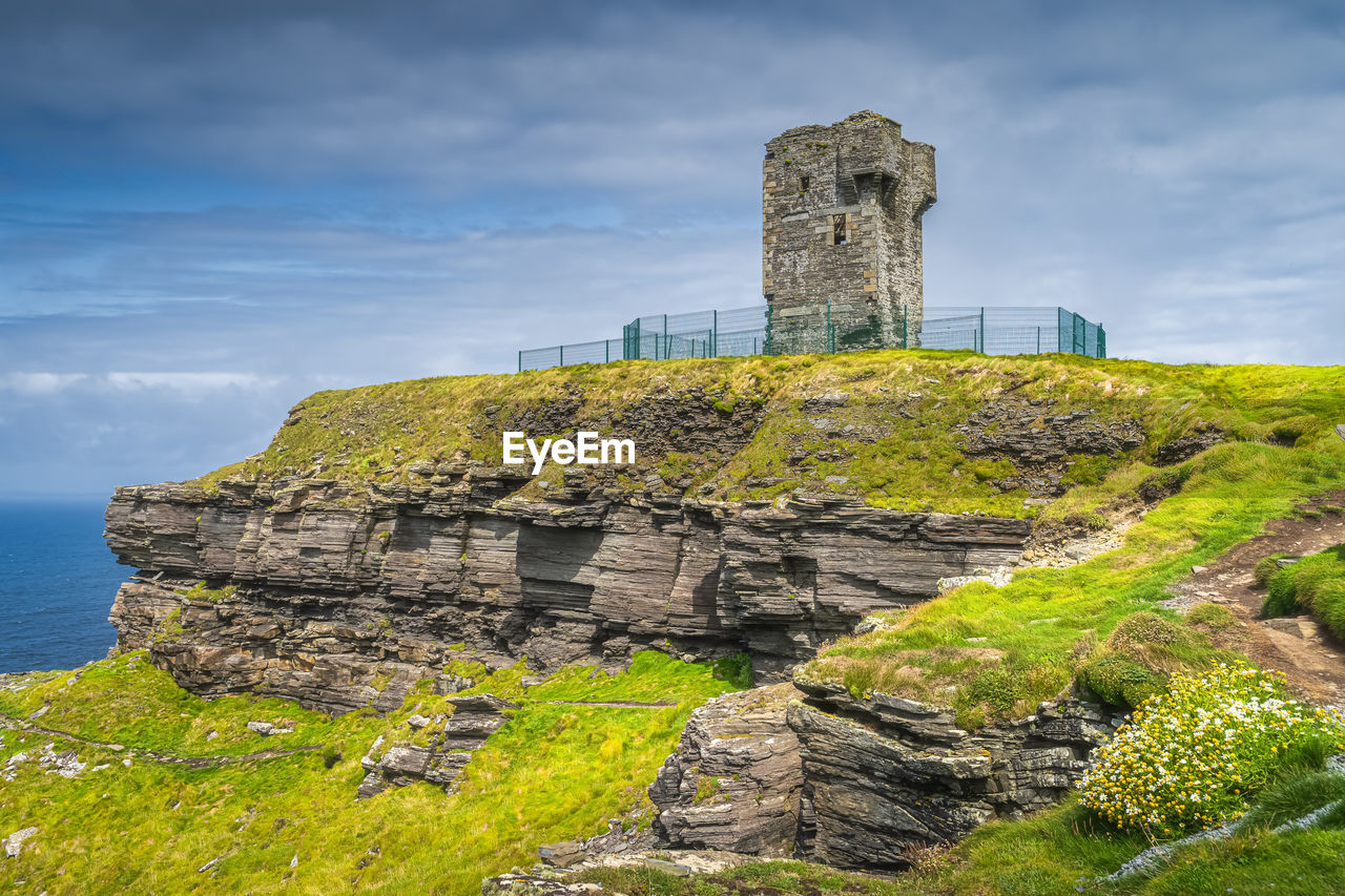 history, the past, architecture, ruins, sky, rock, coast, built structure, travel destinations, cliff, landmark, nature, cloud, fortification, travel, old ruin, land, castle, sea, ancient, hill, tower, water, tourism, building exterior, no people, building, archaeological site, plant, scenics - nature, landscape, old, environment, outdoors, grass, terrain, stone material, beauty in nature, fort, ancient history, ruined, wall, medieval, day, beach, ancient civilization, tranquility, rural area, coastline, château, protection