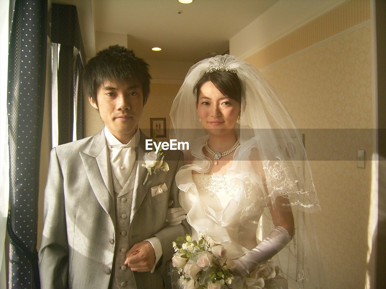 Portrait of smiling bride and groom standing by window