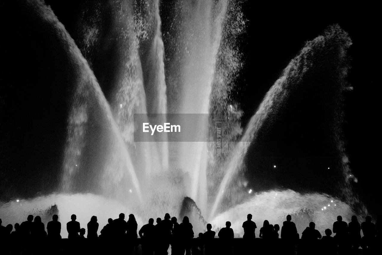 Silhouette crowd standing against illuminated fountain at night