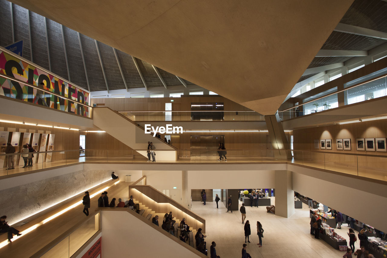 HIGH ANGLE VIEW OF PEOPLE WALKING IN ILLUMINATED MODERN BUILDING