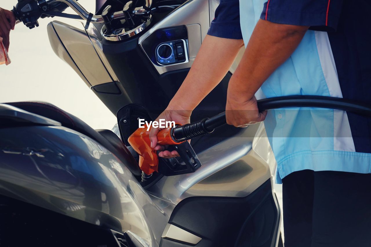 Midsection of man refueling motorcycle at gas station