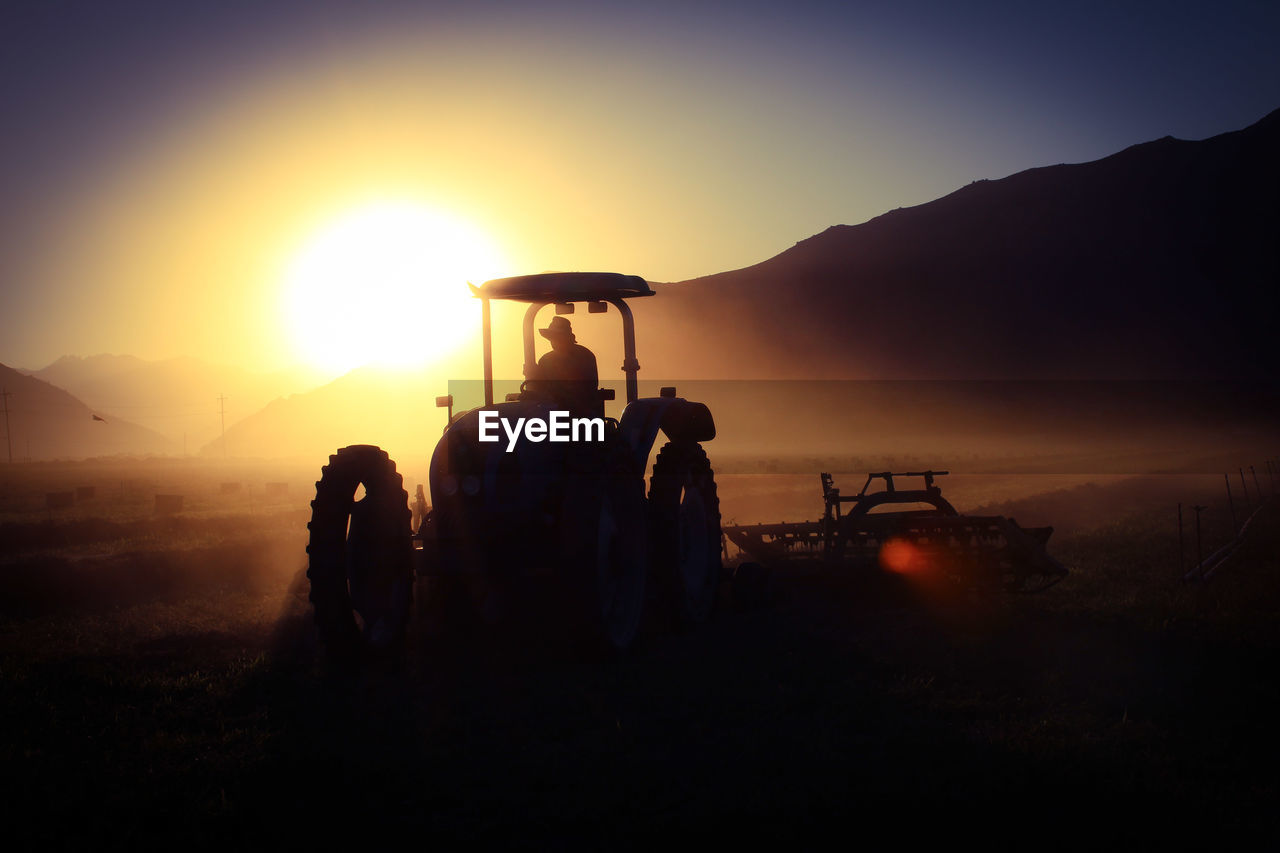 Silhouette people on tractor against mountain ragainst sky during sunrise 