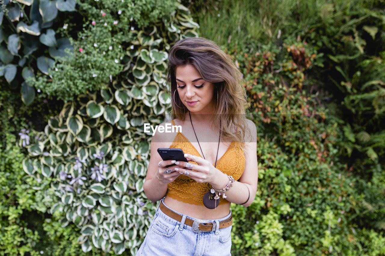 Beautiful woman using phone while standing against plants at park