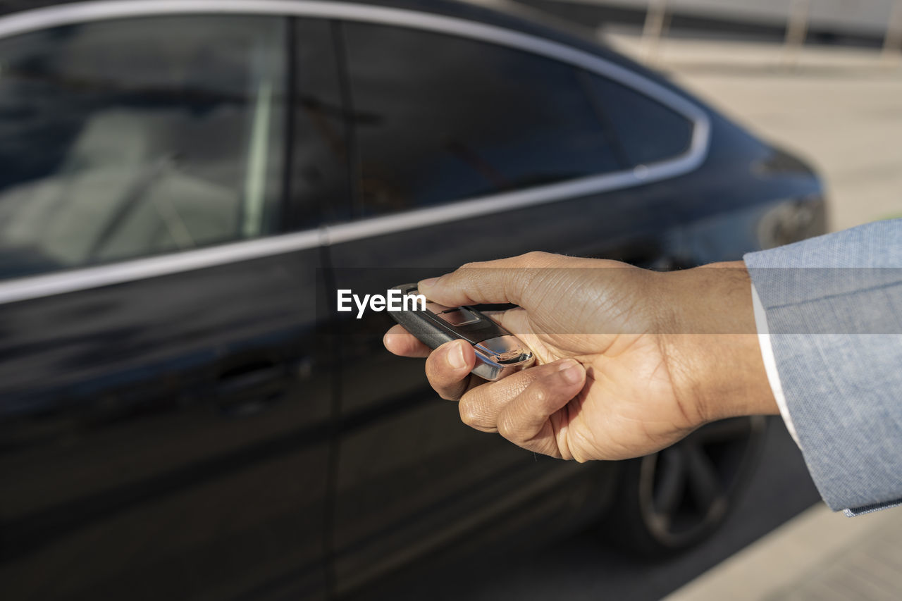 Businessman unlocking car with key on sunny day