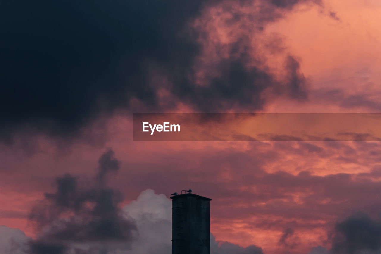 Low angle view of silhouette factory against sky during sunset