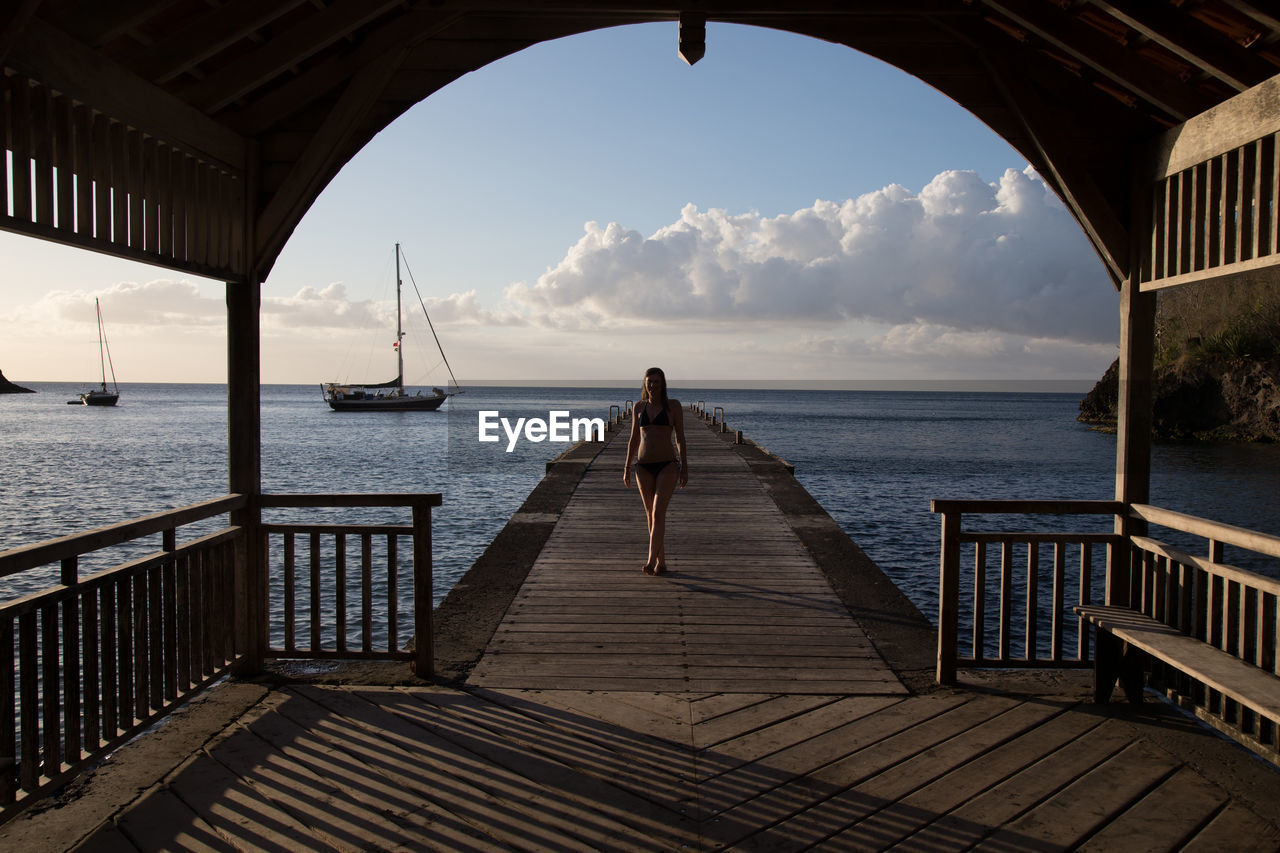 Woman in bikini walking on pier over sea seen from gazebo