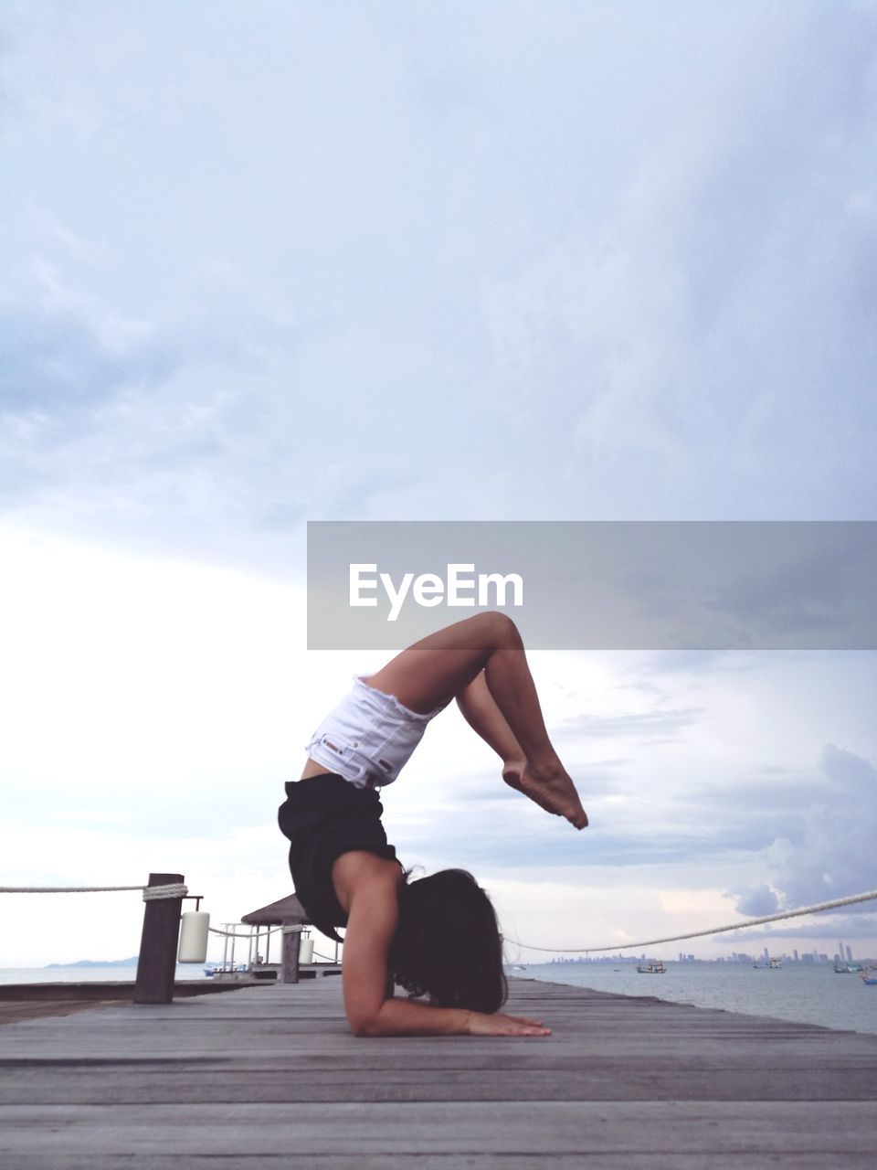 Woman exercising on pier over sea against sky