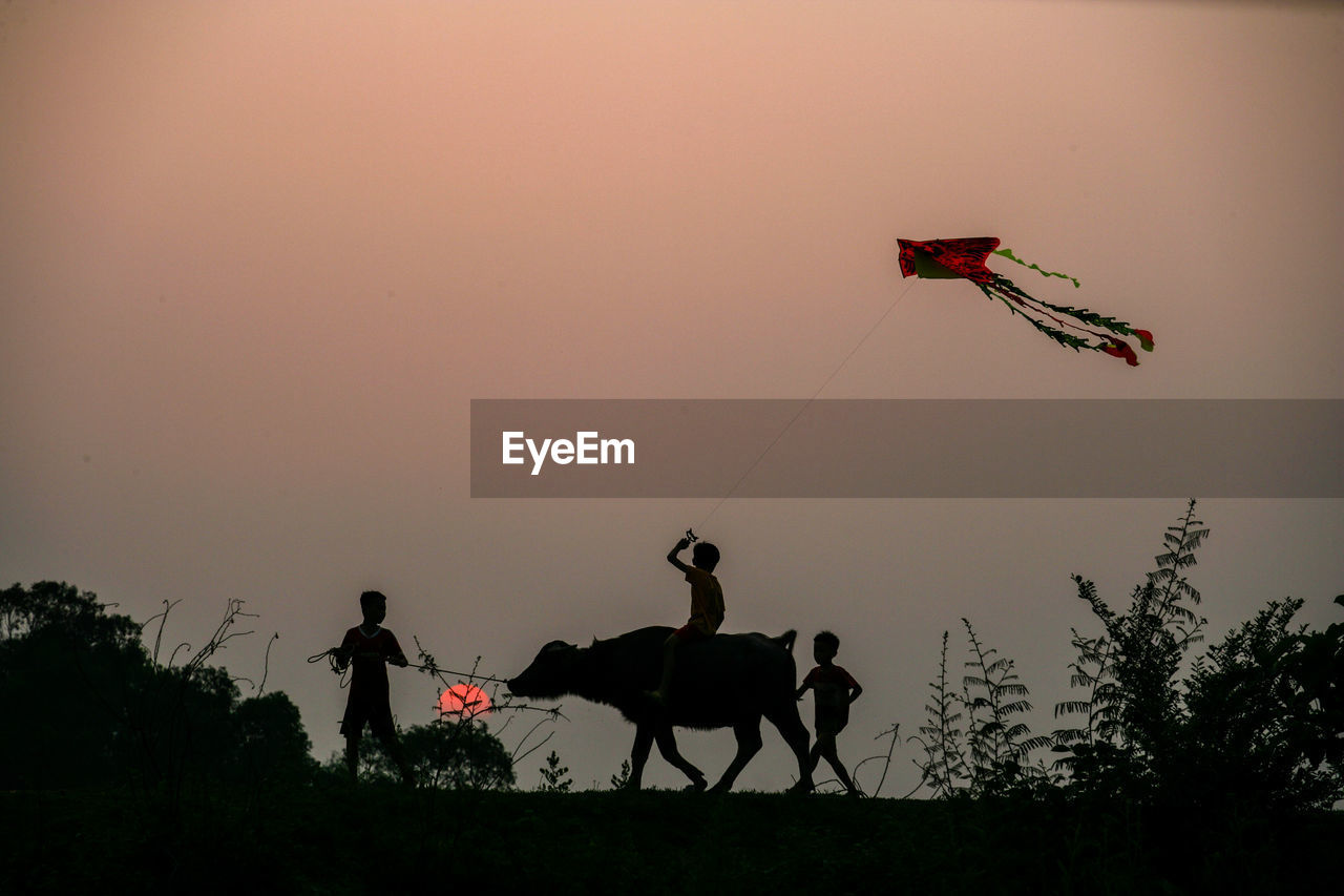 MEN RIDING BICYCLE ON FIELD AGAINST SKY