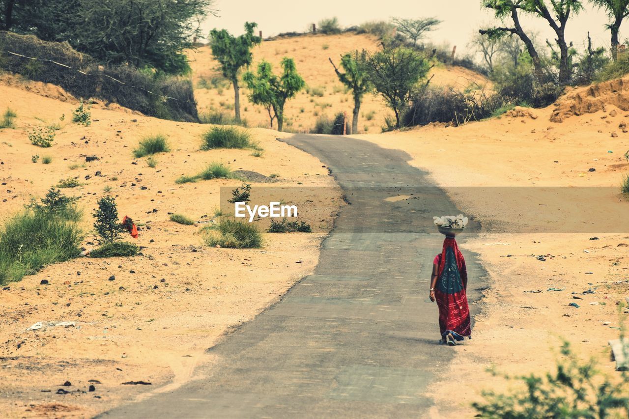 Rear view of woman walking on road at field