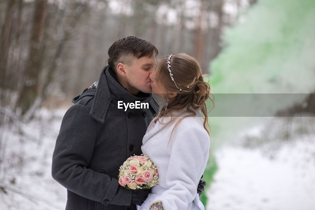 Man kissing woman while holding bouquet during winter