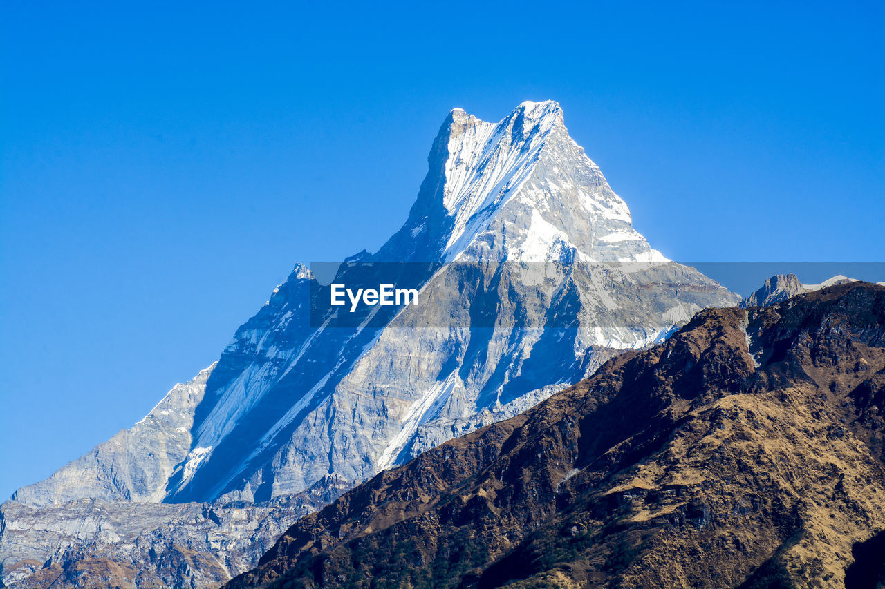 Low angle view of snowcapped mountains against clear blue sky