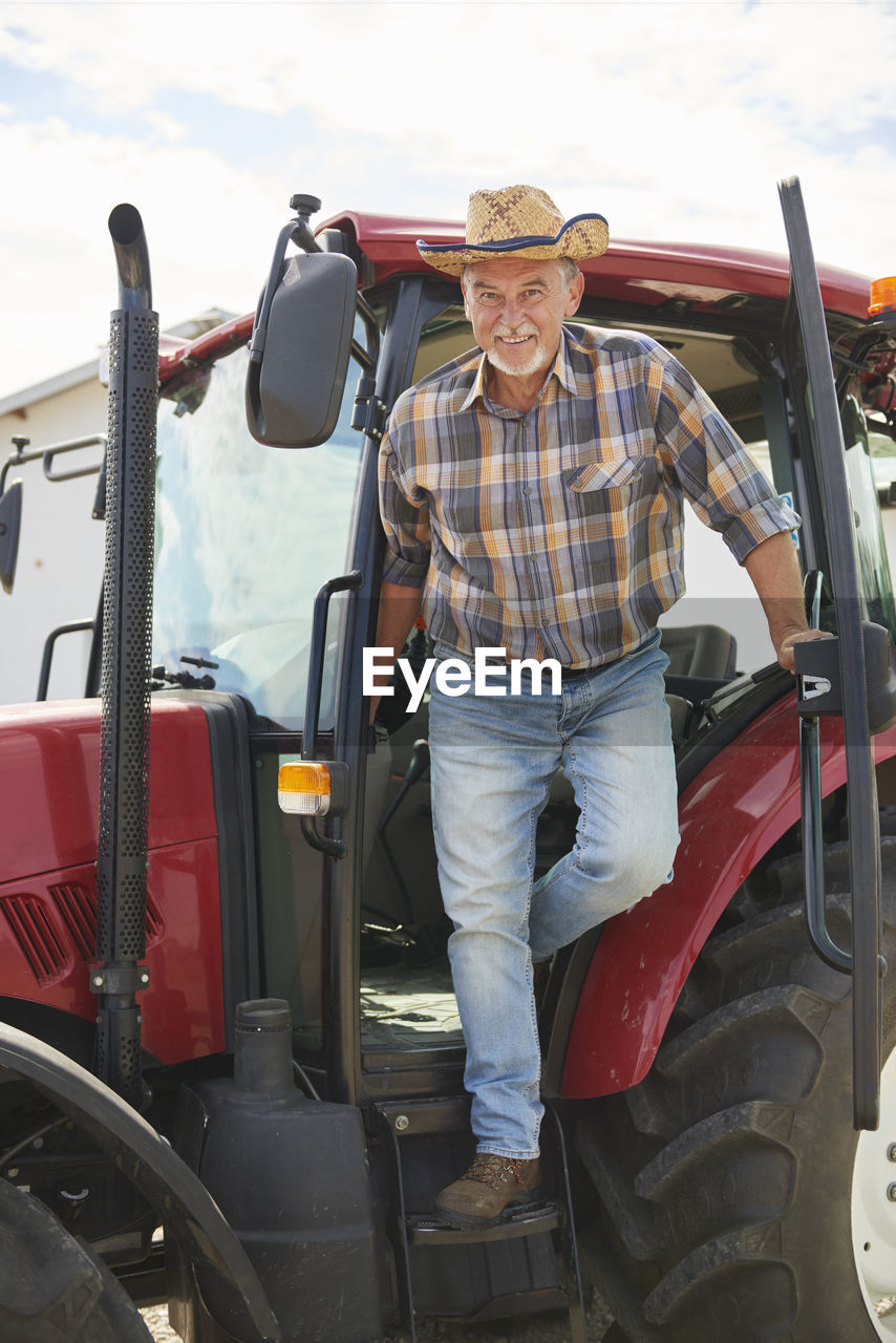 Portrait of smiling senior farmer getting out of tractor