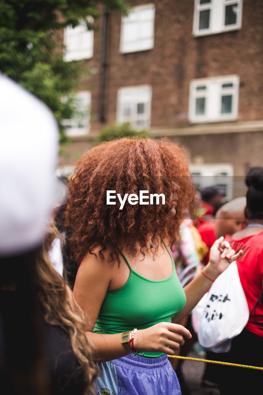 REAR VIEW OF WOMAN STANDING IN FRONT OF PEOPLE