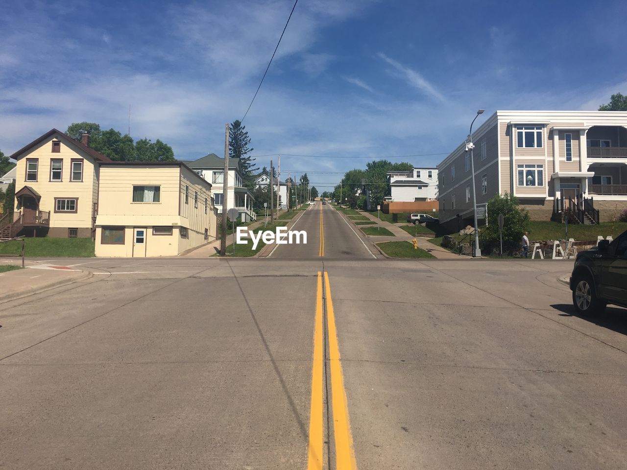 Empty road amidst buildings against sky on sunny day