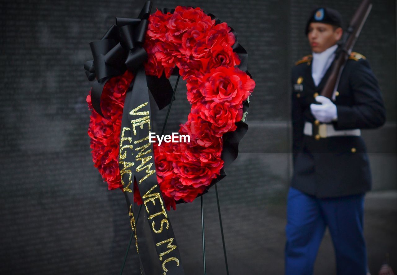 Close-up of red wreath with army soldier standing in background