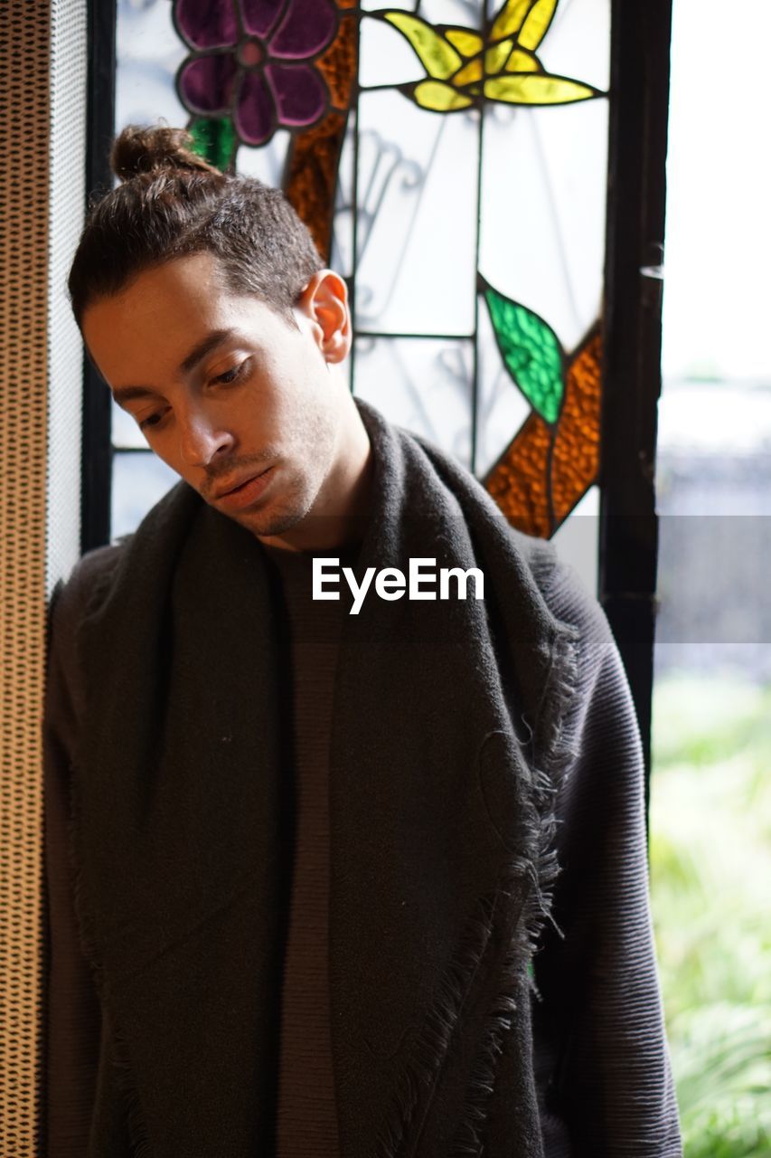 Sad thoughtful young man looking away while standing by window