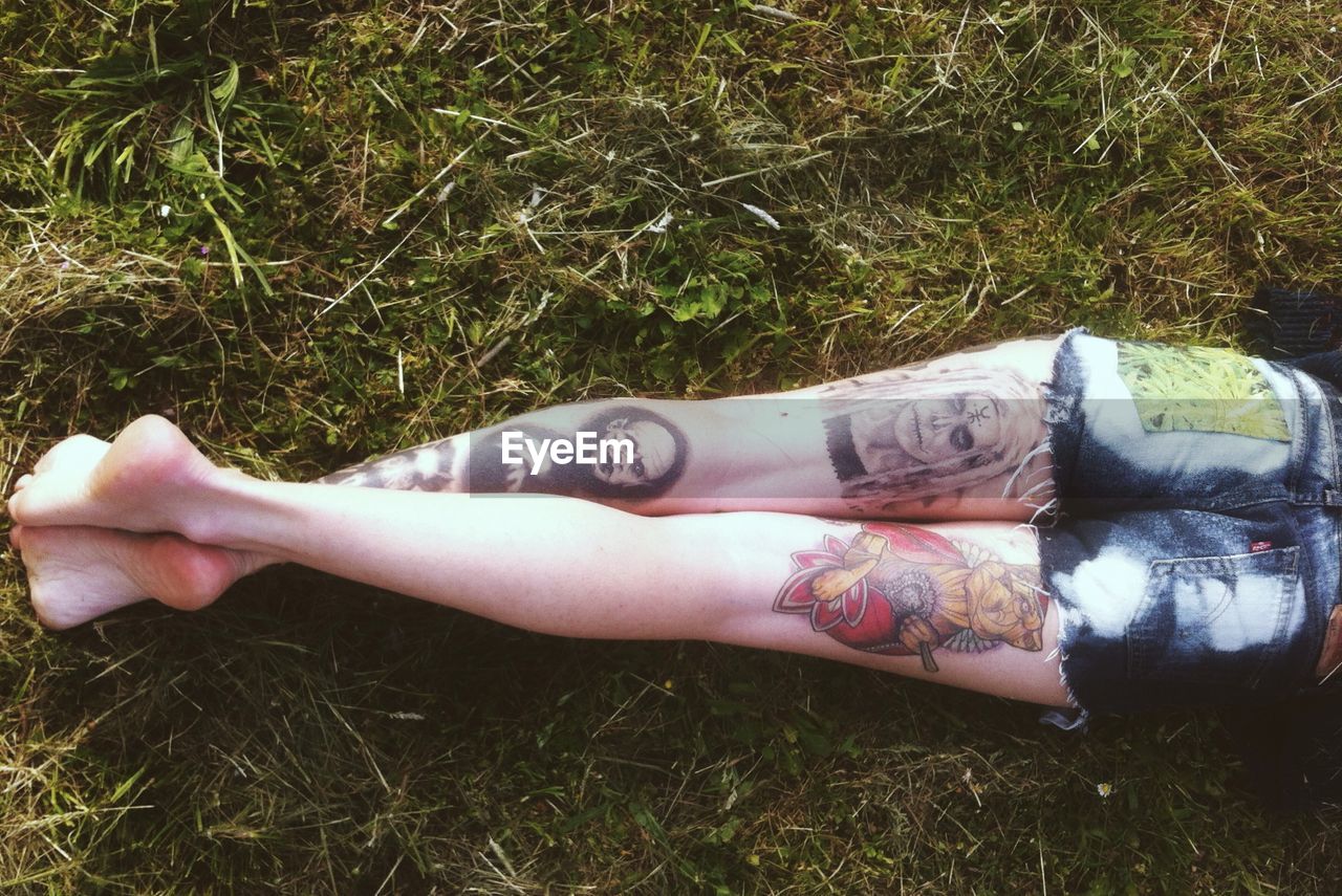 Low section of tattooed woman lying on field