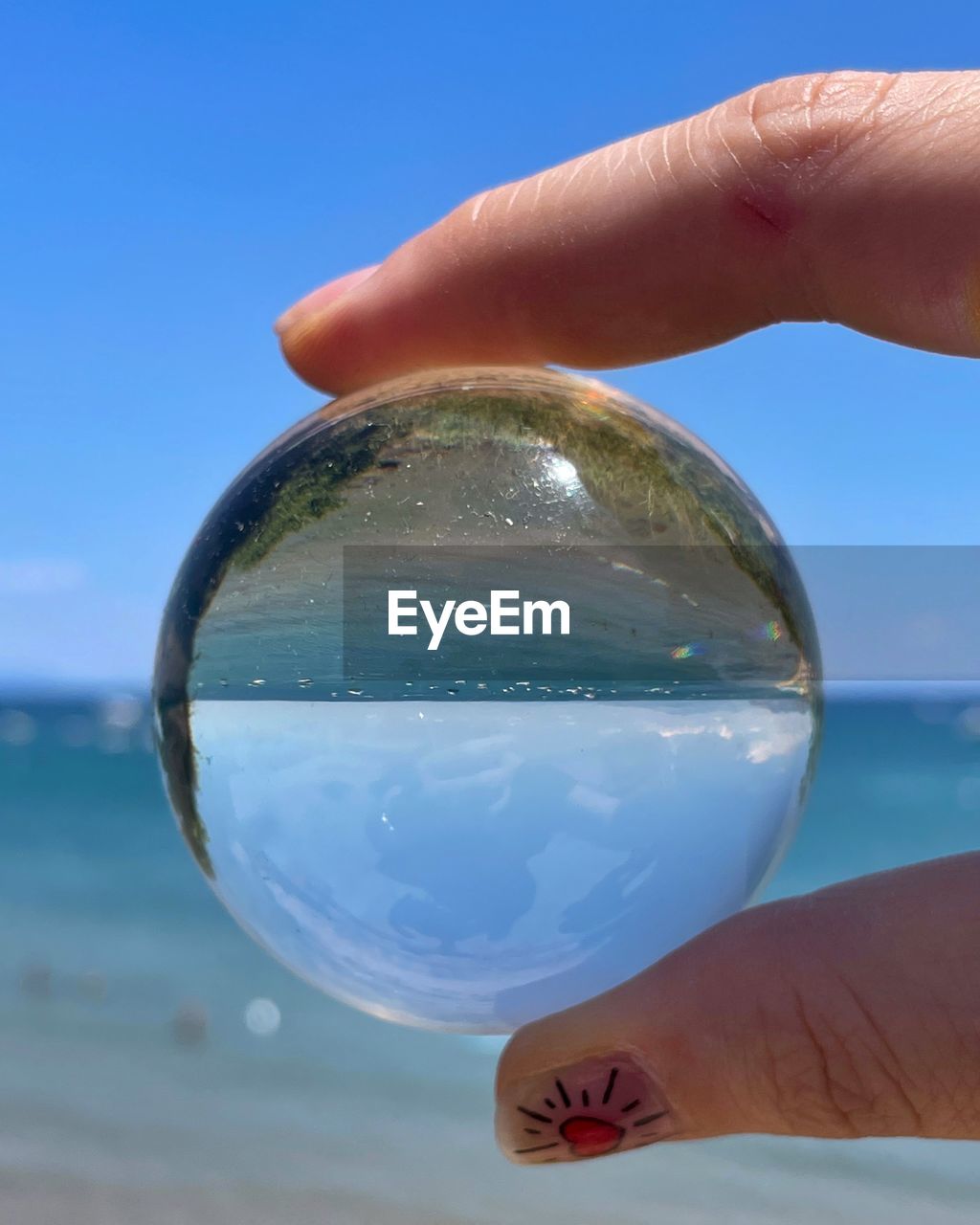 hand, blue, sky, nature, sphere, holding, one person, water, transparent, sea, land, close-up, crystal ball, reflection, clear sky, outdoors, beach, finger, day, adult, focus on foreground, glass, shape, sand, fortune telling, sunlight, environment, holiday