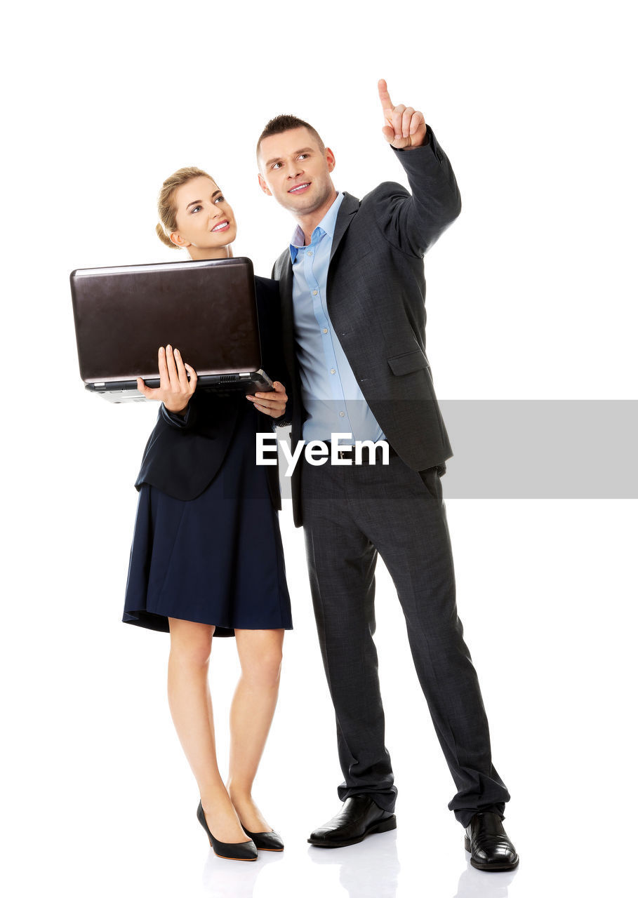 Businesswoman holding laptop while standing by colleague against white background