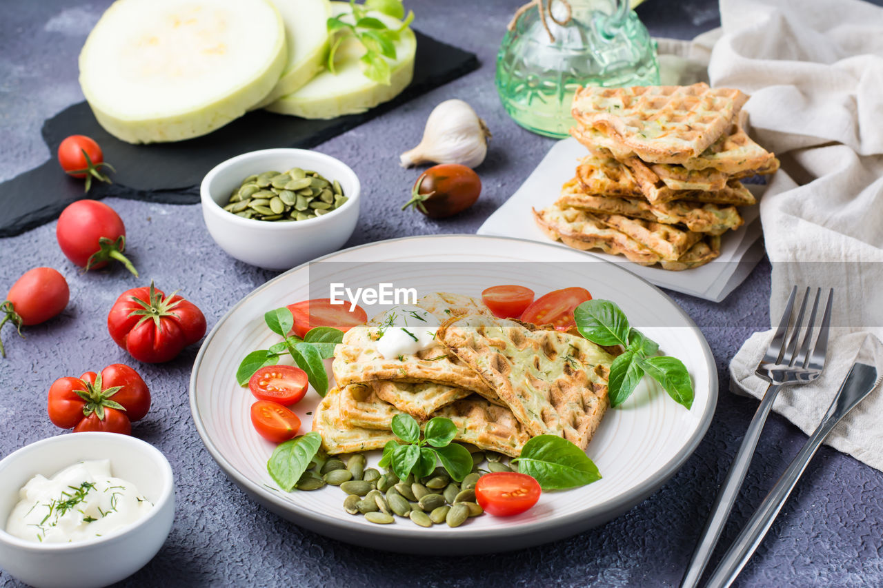Ready-to-eat delicious zucchini waffles, tomatoes, basil and pumpkin seeds on a plate on the table