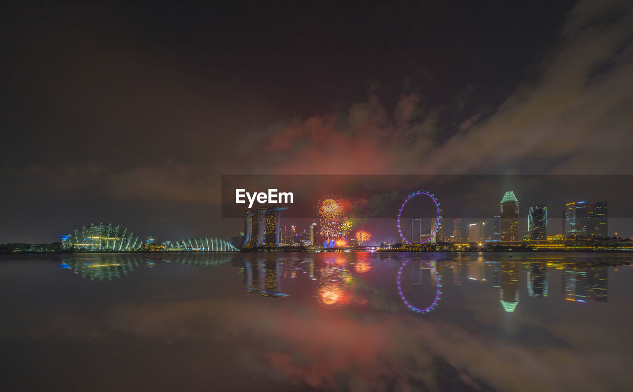 Marina bay sands and ferris wheel reflecting on bay of water in city at night