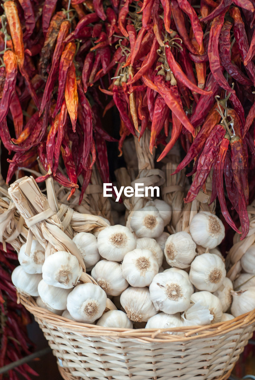 Close-up of garlic cloves in wicker basket amidst dried red chili peppers at market stall