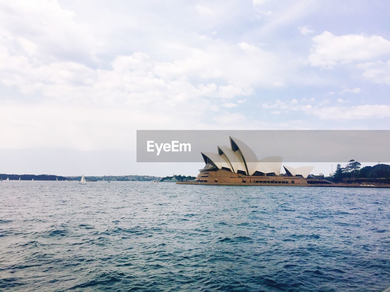 Sydney opera house by sea against cloudy sky