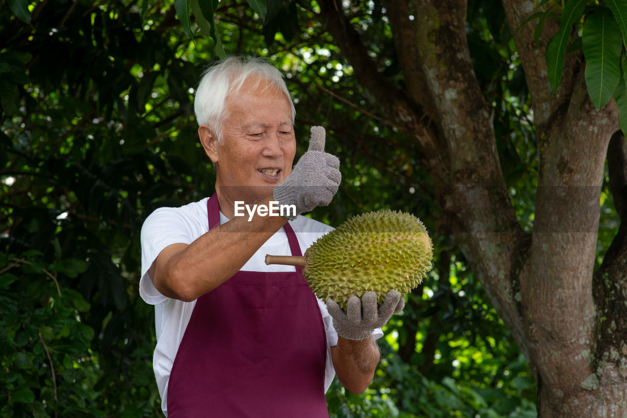 Man holding durian while standing against trees