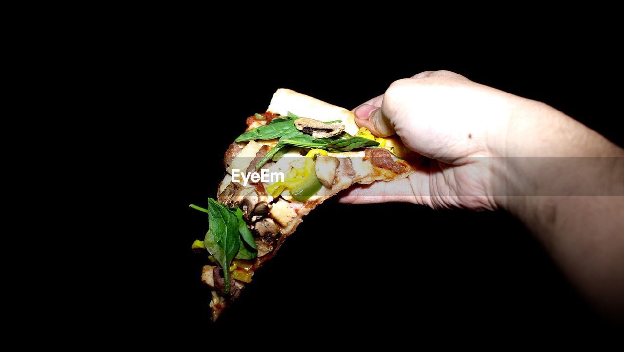 Cropped hand holding pizza slice against black background