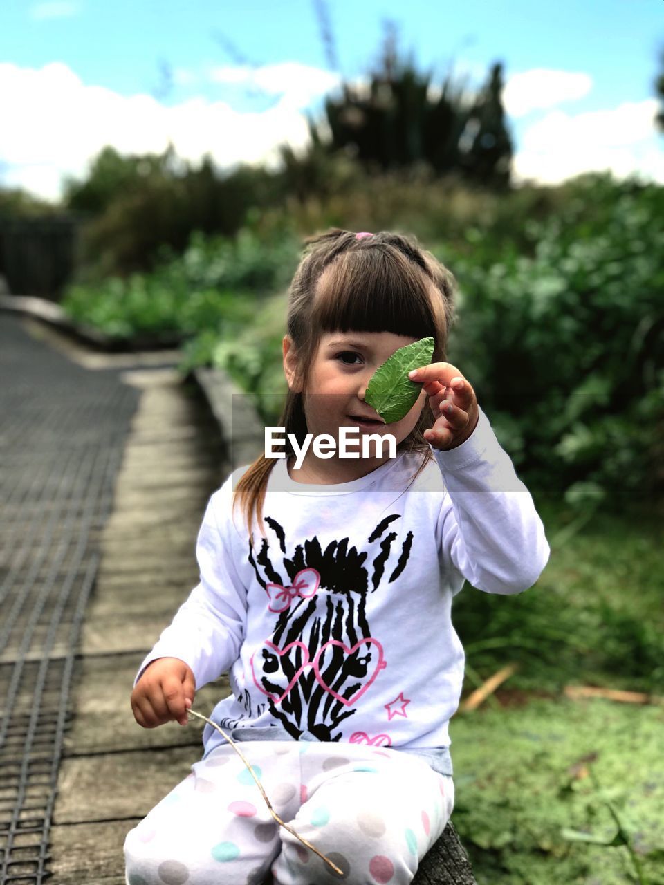 Portrait of girl holding leaf while sitting against plants