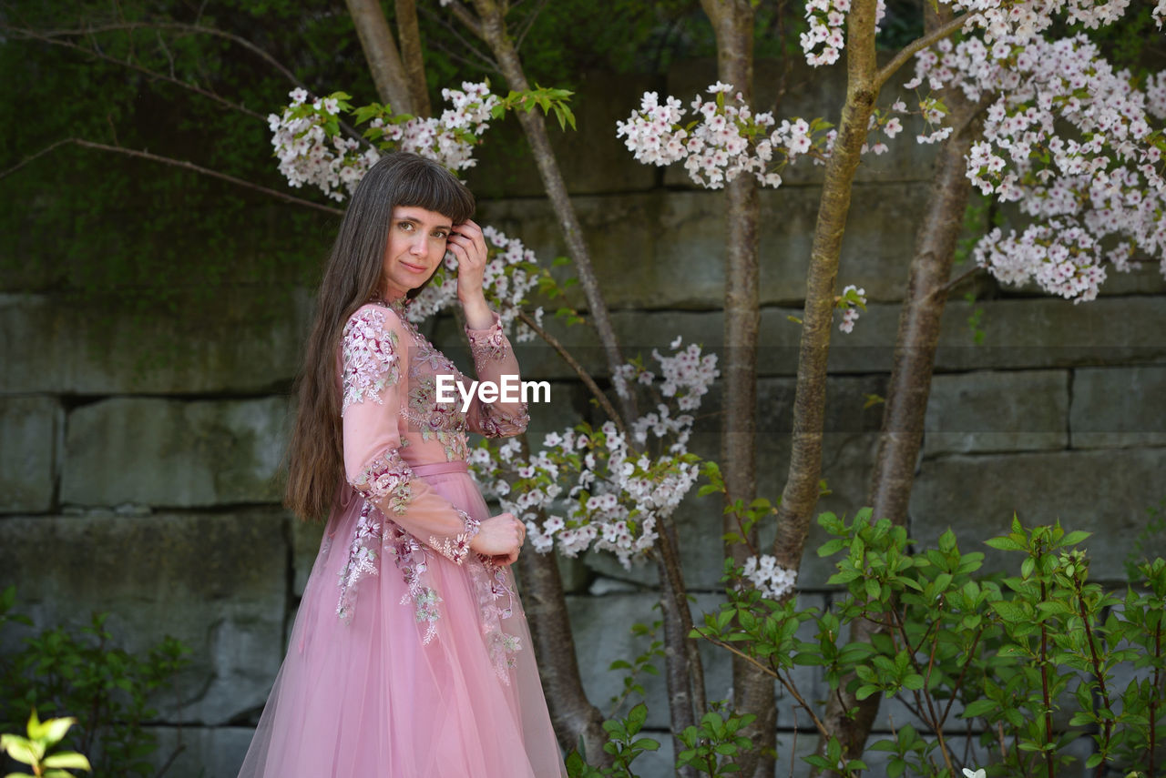 MIDSECTION OF WOMAN STANDING BY PINK FLOWERING PLANT