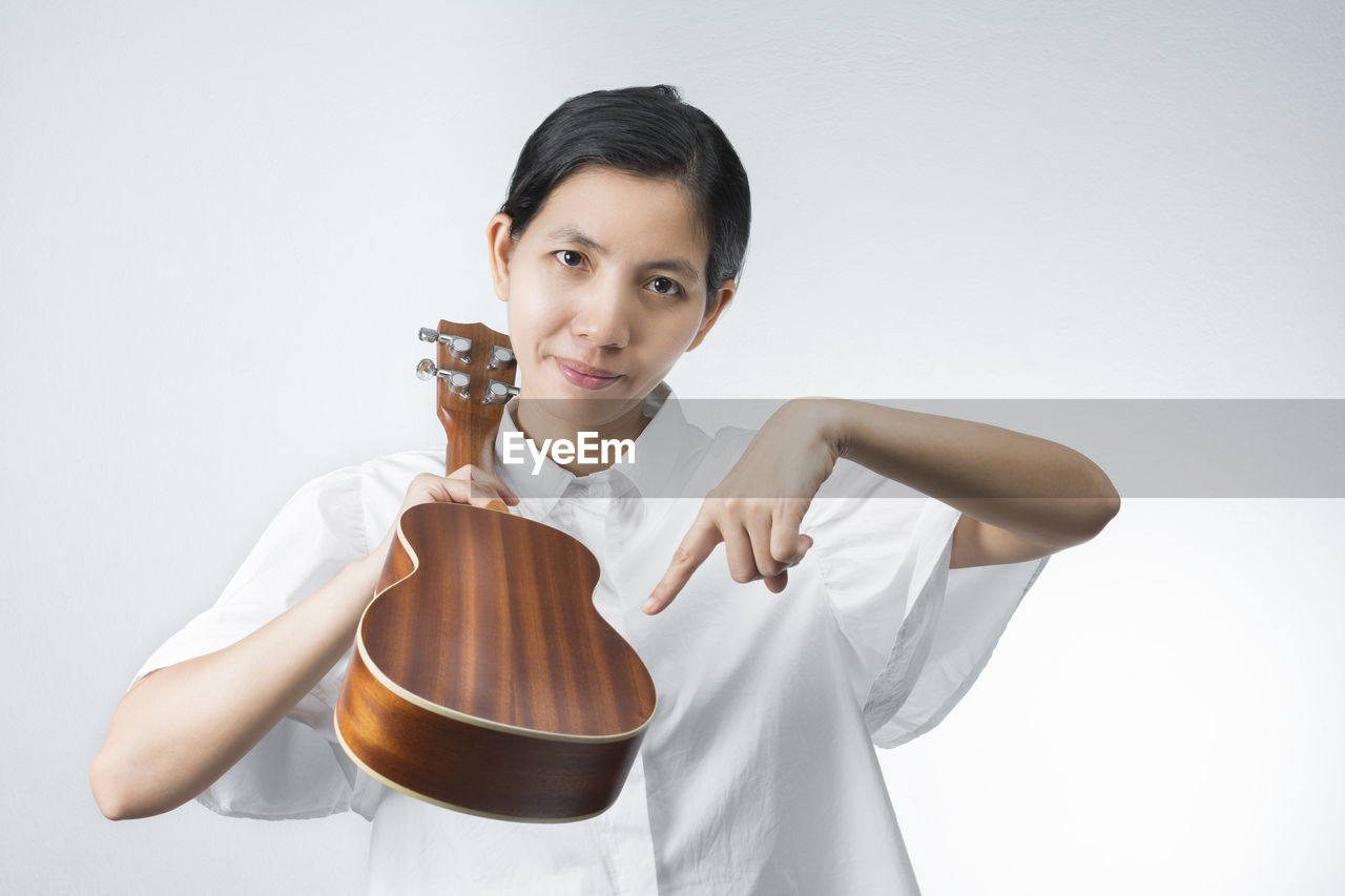 Portrait of woman pointing at guitar against white background