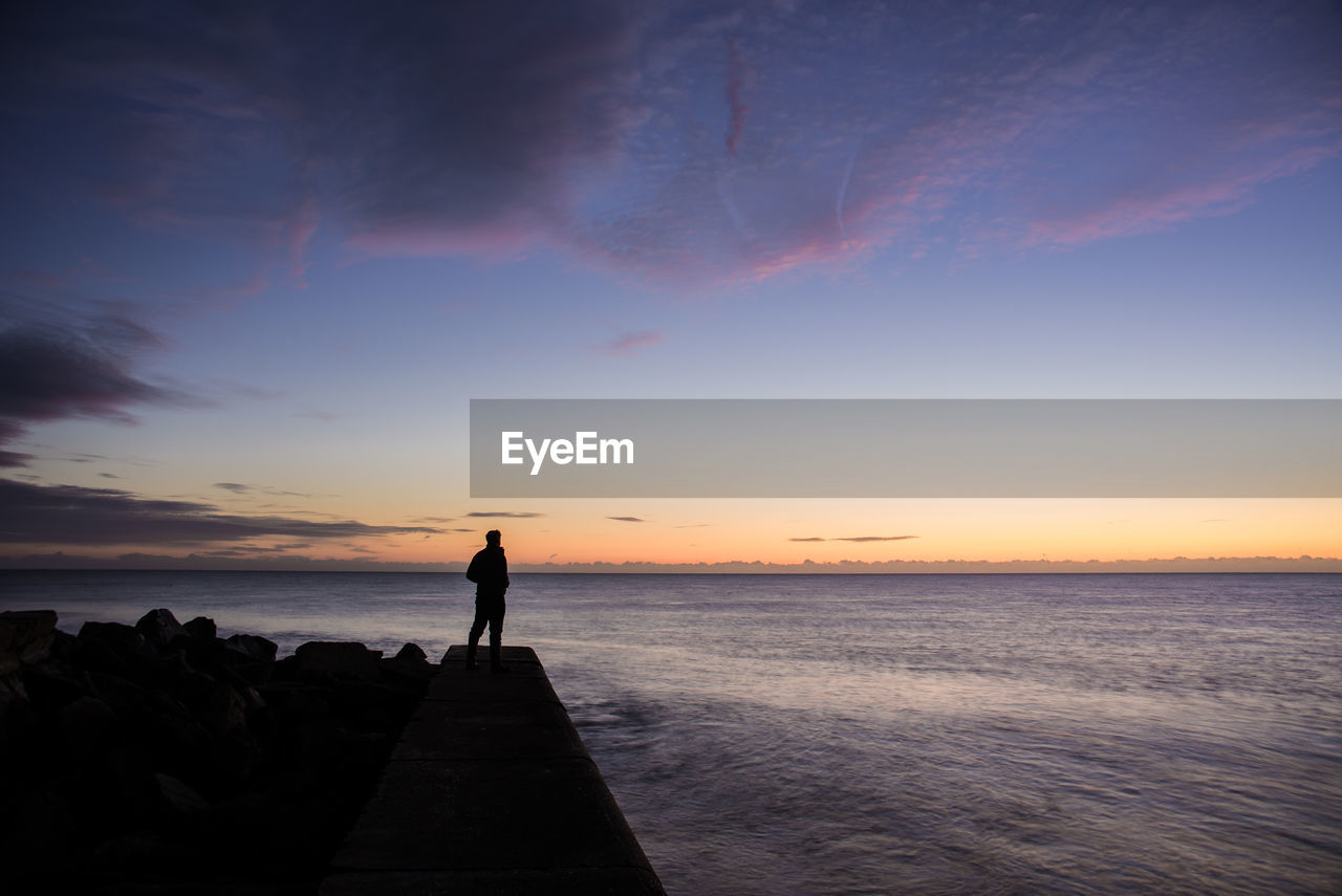 Silhouette man standing at beach against sky during sunset